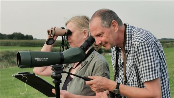 Ein Mann und eine Frau gucken durch ein Spektiv und ein Fernglas.