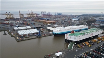 Auf dem Bild ist das Autoterminal in Bremerhaven zu sehen, im Hintergrund stehen Kräne des Containerterminals.