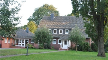Ein Haus steht am Ende einer Wiese zwischen Bäumen.