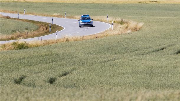 Ein Polizeiwagen fährt auf einer Straße durch Landwirtschaftliche Nutzfläche.