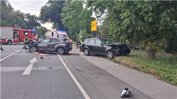 Zwei verunfallte Autos stehen auf einer Straße. Im Hintergrund sind Fahrzeuge der Feuerwehr.