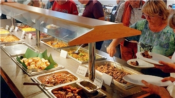 Eine ältere Frau schöpft mit einer Kelle Essen aus einem Behälter.