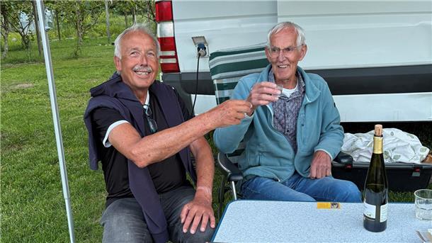 Zwei Männer sitzen nebeneinander und prosten sich zu.