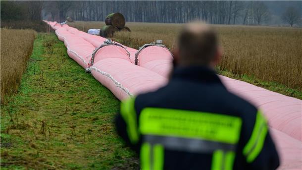 Auf einem Feld liegt ein Teil von einem mobilen Deich, welcher mit Wasser befüllt ist.
