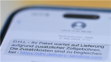 Auf einem Smartphone ist eine Betrugs-SMS zu lesen, in der Kriminelle ein Paket ankündigen und dafür Zollgebühren einfordern. Die Deutsche Telekom will vom 1. April an solche betrügerischen SMS blockieren.