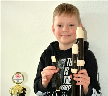 Ein Junge hält drei Blockflöten in der Hand. Neben ihm steht ein Pokal. 