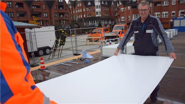Zwei Männer tragen auf dem Nordenhamer Marktplatz eine weiße Kunststoffplatte.