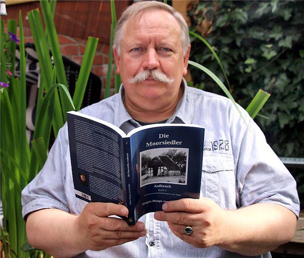 Jürgen Hoops hält sein Buch in den Händen und schaut in die Kamera.