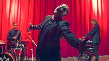 Drei Musiker der Nordenhamer Band Ultraviolett in schwarzen Anzügen, Frontmann Niklas Kanthack mit Gesichtsmaske und ausgebreiteten Armen im Vordergrund.