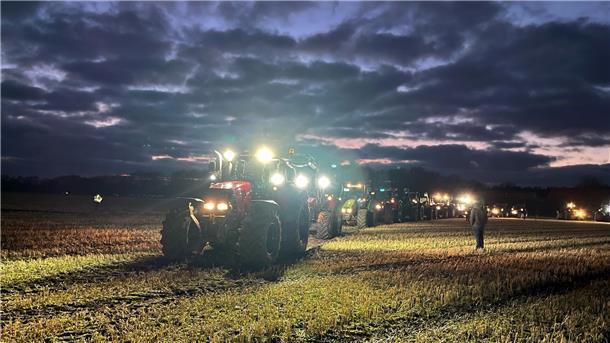 Beleuchtete Traktoren fahren zur Abendzeit auf eine Weide