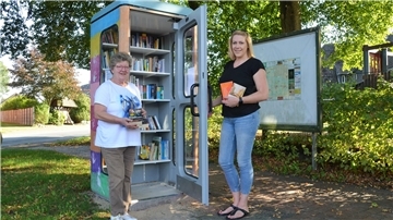 Marlies Stuthmann und Sarah Ohlberger halten vor dem Offenen Bücherschrank in Bramel Bücher in Händen