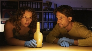 Antonia Bill und Oliver Mommsen schauen sich eine Flasche an.