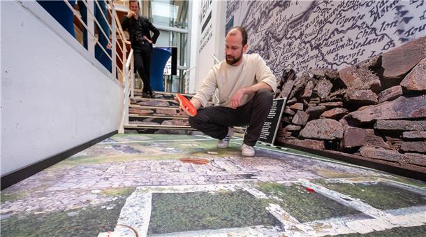 Ausstellung mit "doppeltem Boden": Dr. Philipp Grassel hebt ein Info-Puzzleteil hoch. Unter ihm ist die archäologische Grabungsstätte auf den Shetland-Inseln dargestellt. 