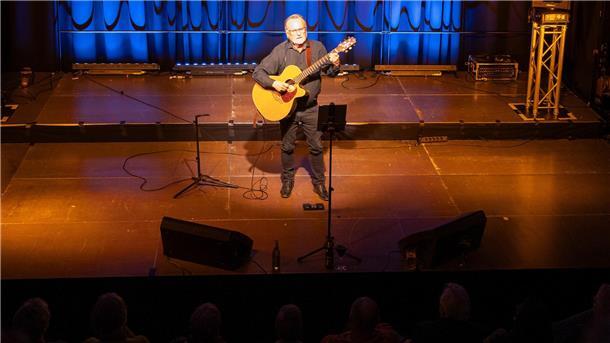 So stimmungsvoll war das Konzert mit Hartmut Becker in der Nordenhamer Jahnhalle Ein Mann steht mit Gitarre auf einer stimmungsvoll beleuchteten Kleinbühne.