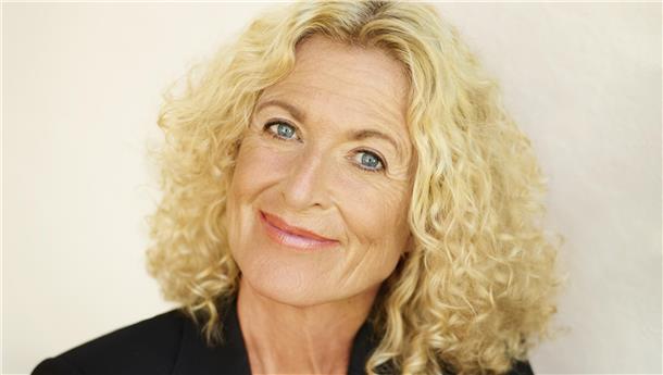 Eine Frau mit blonden Haaren lächelt freundlich.