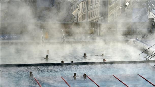 Badegäste schwimmen am frostigen Morgen draußen im Freibad eines Thermalhotels in Karlsbad in Tschechien.