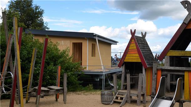 Sanierung am Bederkesaer Kanal: Die Stege sind fertig Auf einem sandigen Bogen stehen Spielgeräte für Kinder. Ein kleines Gebäude befindet sich im Bau.