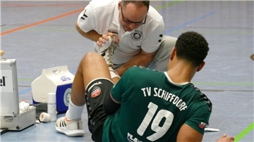 Handballer Joel Hoppe liegt verletzt am Boden und wird von Physiotherapeut Alexander Müller-Porwoll behandelt.