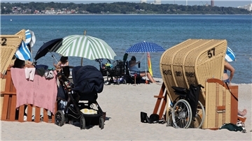 Zwei Strandkörbe am Strand mit einem Rollstuhl und einem Kinderwagen.