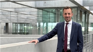 Ein Mann mit Anzug steht im Deutschen Bundestag und guckt in die Kamera.