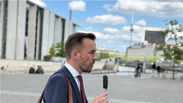 Ein Mann mit Anzug geht durch Berlin. In der Hand hält er ein Eis am Stiel. 