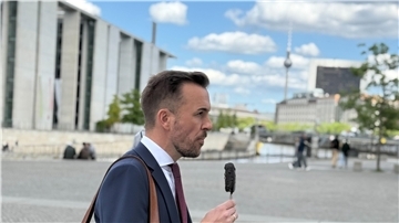 Ein Mann mit Anzug geht durch Berlin. In der Hand hält er ein Eis am Stiel. 