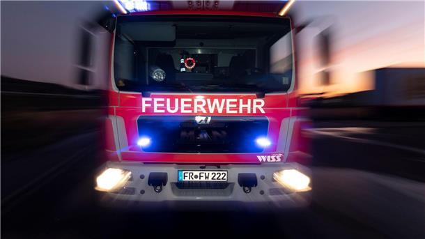  Ein Feuerwehrfahrzeug steht mit eingeschaltetem Blaulicht im Sonnenuntergang auf einer Straße. 