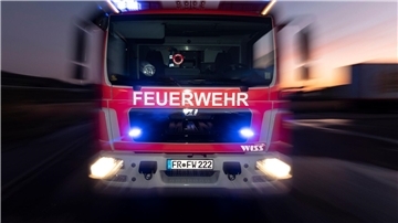  Ein Feuerwehrfahrzeug steht mit eingeschaltetem Blaulicht im Sonnenuntergang auf einer Straße. 