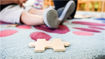 Ein Puzzleteil aus Holz liegt auf einem Teppich in einer Kita.