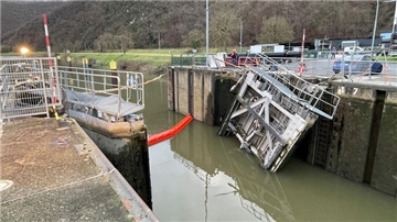 Ein Bild von einer beschädigten Schleusenanlage, bei der ein Teil des Schleusentores in das Wasser gefallen ist. Ein roter schwimmender Ölsperrenabschnitt befindet sich im Wasser.