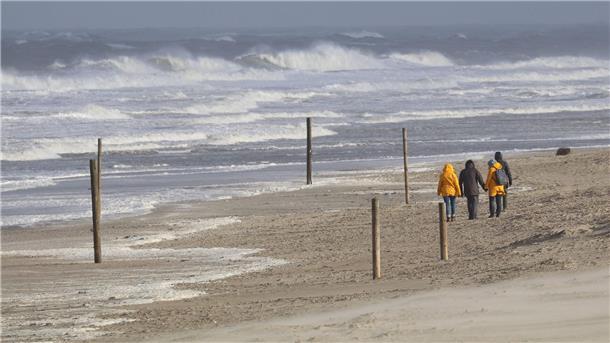 Bei stürmischem Wetter und Wellen gehen Spaziergänger am Strand entlang.