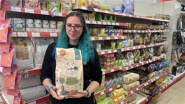 Eine Frau steht vor einem Regal mit Hundefutter. Sie hält einen Sack Trockenfutter in den Händen.