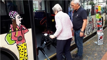 Eine Frau mit Rollator steigt in einen Bus. 