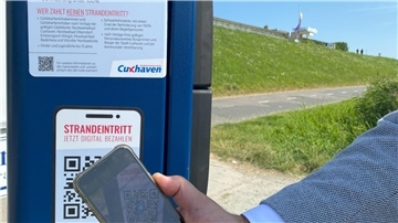 Eine Person scannt einen QR-Code am Strand.