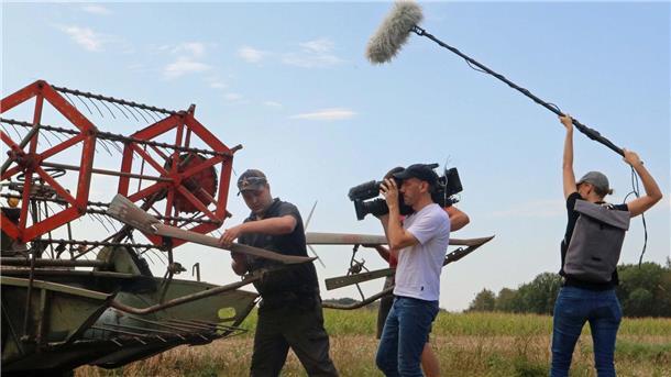 Ein Mann an einem Mähdrescher wird von einem Kamerateam gefilmt.