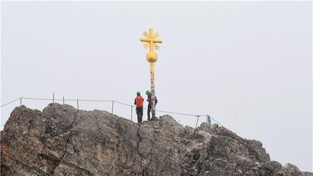 Bergsteiger stehen neben dem Gipfelkreuz des Zugspitzgipfel.
