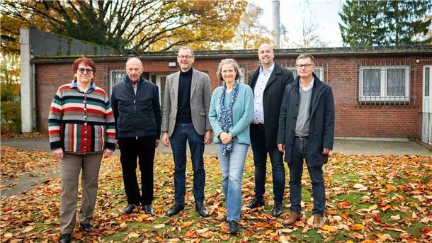 Zwei Frauen und vier Männer stehen nebeneinander auf einer Rasenfläche. Im Hintergrund ein Gebäude.