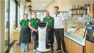 Drei Menschen stehen zusammen mit einem Service-Roboter vor einer Eistheke.