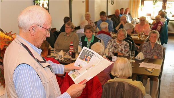 Hans-Dieter Lüerssen liest stehend aus seinem Buch vor, während die Teilnehmer der Veranstaltung an Tischen sitzen und zuhören.