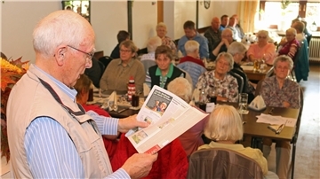Hans-Dieter Lüerssen liest stehend aus seinem Buch vor, während die Teilnehmer der Veranstaltung an Tischen sitzen und zuhören.