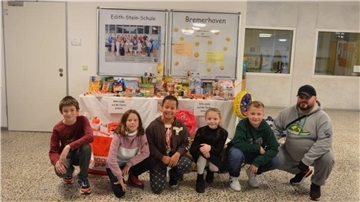 Klassensprecher der 5. Klassen der Edith-Stein-Schule und Silvio Späte vom Verein "Rückenwind für Leher Kinder" knien vor dem Gabentisch mit den gespendeten Lebensmitteln, Büchern, Spielzeug und Bekleidung