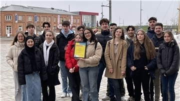 8. Klasse steht zusammen am Neuen Hafen in Bremerhaven, eine Schülerin hält eine gerahmte Urkunde in Händen