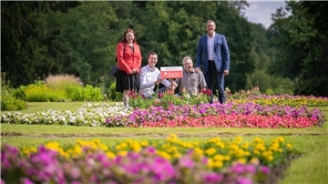 Eine Frau und drei Männer stehen oder knien nebeneinander inmitten bunter Blumenbeete