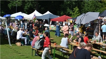 Menschen sitzen an Biertischgarnituren im Zevener Stadtpark. Im Hintergrund Pavillons