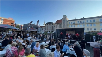 Vielen Menschen sitzen an Tischen vor einer Bühne.