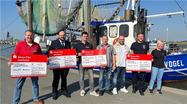 Menschen vor einem Krabbenkutter halten Spendenschecks in den Händen