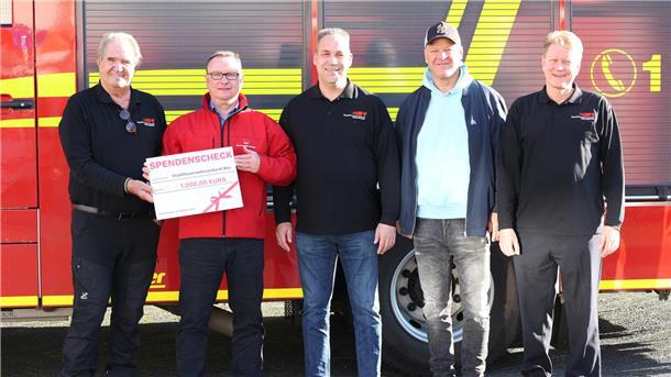 Gruppenfoto mit Spendenscheck Fünf Männer vor einem roten Feuerwehrfahrzeug