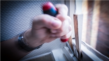 Ein Einbrecher hebelt ein Fenster aus
