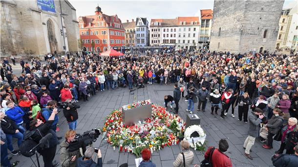 Menschen stehen in Halle um niedergelegte Blumen