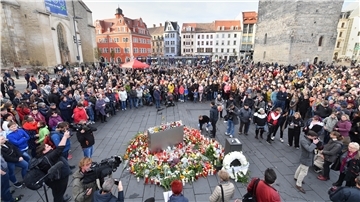 Menschen stehen in Halle um niedergelegte Blumen